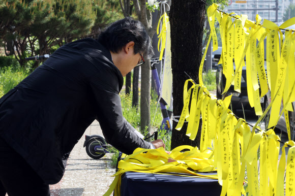 7일 고교생 흉기 살인사건이 발생한 광주 광산구 월계동 현장에 마련된 추모공간에서 한 시민이 노란 리본에 애도 메시지를 적고 있다. 2026.5.7 연합뉴스