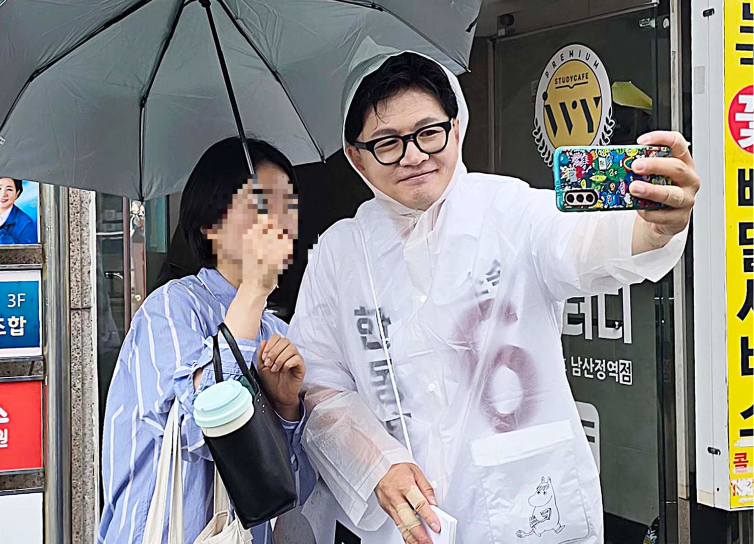 무소속으로 부산 북구갑 국회의원 보궐선거에 나선 한동훈 후보가 북구 남산정역 출구 앞에서 우비를 입고 주민과 사진을 찍고 있다.