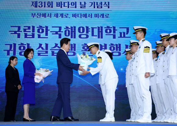 이재명 대통령이 27일 부산 영도구에서 열린 제31회 바다의 날 기념식에서 귀항 보고를 한 해양대 실습생에게 꽃다발을 주고 있다. 2026.5.27 연합뉴스