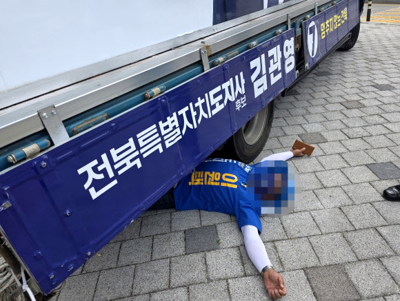 1일 오전 전북 전주시 완산구의 한 네거리에서 더불어민주당 이원택 전북특별자치도지사 후보의 선거운동원이 무소속 김관영 후보 유세차 밑으로 들어가 드러누워 있다. 2026.6.1. 연합뉴스