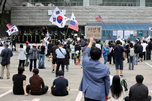 6·3 지방선거 투표용지 부족 사태를 규탄하며 재선거를 요구하는 ‘잠실 개표소 봉쇄 시위’가 계속되고 있는 8일 서울 송파구 올림픽공원 핸드볼경기장 출입구 앞에서 참가자들이 구호를 외치고 있다. 2026.6.8  연합뉴스
