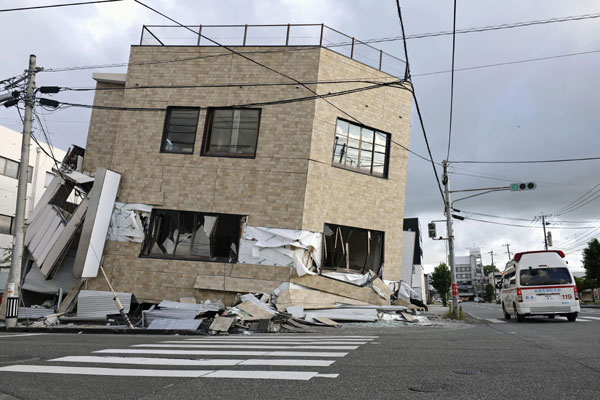 29일 일본 규슈 서부 구마모토현 야쓰시로에서 구급차 한 대가 전날 발생한 지진으로 주저앉은 건물 옆을 지나고 있다. AP 뉴시스