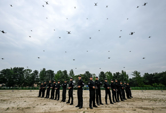 육군은 28일 경기 이천 육군정보학교에서 ‘드론·로봇 전술시범단’ 창설식을 개최했다고 밝혔다. ‘드론ㆍ로봇 전술시범단’은 대내외 주요행사에서 드론 전술비행과 군집비행, 다족형로봇과 무인차량 등 유무인복합전투체계 운용을 선보인다. 드론ㆍ로봇 전술시범단 장병들이 군집비행 중인 드론을 배경으로 기념 촬영하고 있다. 2026.8.28. 육군 제공