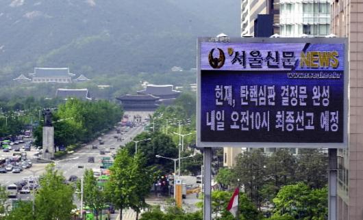 긴장속의 청와대 헌법재판소의 노무현 대통령 탄핵소추안 결정을 하루 앞둔 13일 본사 대형 전광판이 관련 뉴스를 보도하고 있다.광화문앞을 무심히 오가는 차량들 너머 왼쪽으로 청와대가 멀리 보인다. 이호정기자 hojeong@