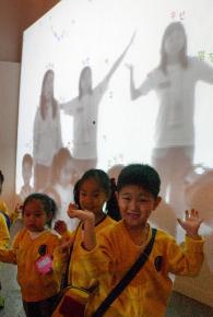 아이들이 '글자비' 놀이터 앞에서 스크린 속 흘러내리는 글자를 받으며 웃고 있다.