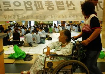 환자고통 외면하고…  전국보건의료산업노조가 총파업에 들어간 지난 10일 서울 종로구 연건동 서울대병원에서 휠체어를 탄 입원 환자가 무표정하게 집회장 곁으로 지나가고 있다. 서울신문 포토라이브러리