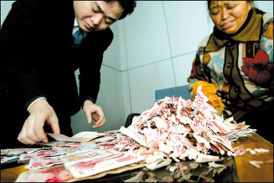 쥐가 물어뜯어 조각조각 난 돈을 정리하고 있는 은행 직원과 뤄씨. 중경상보 