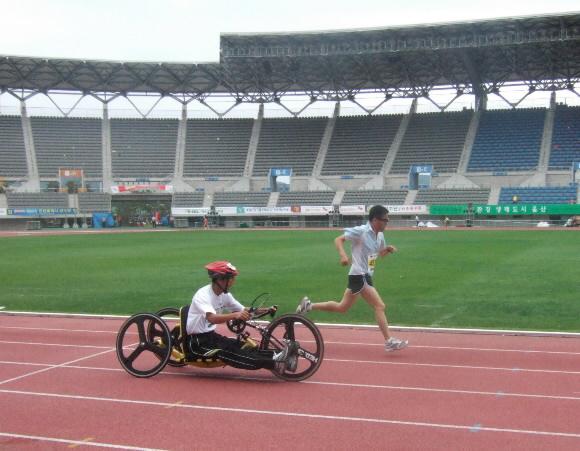 지난해 울산에서 열린 국민생활체육대축전 육상 마라톤에 참가한 핸드바이크 선수와 비장애 선수가 트랙을 힘차게 내닫고 있다. 대한장애인체육회 제공