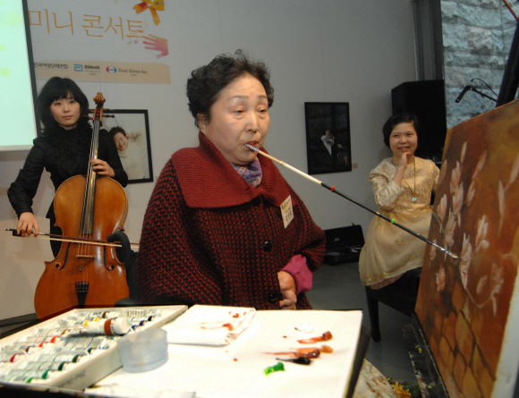 구족화가 김성애(가운데)씨가 4일 서울 강남구 청담동 갤러리 더 스페이스에서 열린 ‘여류사랑 희망공감 전시회’에서 그림을 그리고 있다. 오른쪽은 네 손가락 피아니스트 이희아씨. 대한류마티즘학회 제공 