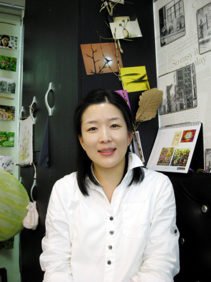 머리카락 그림들이 내걸린 미용실 벽을 배경으로 포즈를 취한 안정숙씨.