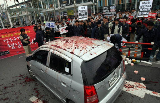  3일 고양시 일산 킨텍스에서 서울모터쇼가 개막된 가운데 전국금속노동조합원들이 행사장 앞에서 기아차 모닝에 소(牛)피를 뿌리는 퍼포먼스를 하고 있다. 조합원들은 현대, 기아, 쌍용, GM대우의 강제휴업 및 대량해고 일자리 빼앗기를 중단하라며 기자회견을 열고 퍼포먼스를 벌이다 전원 출동한 경찰에 연행되었다.   　고양=연합뉴스