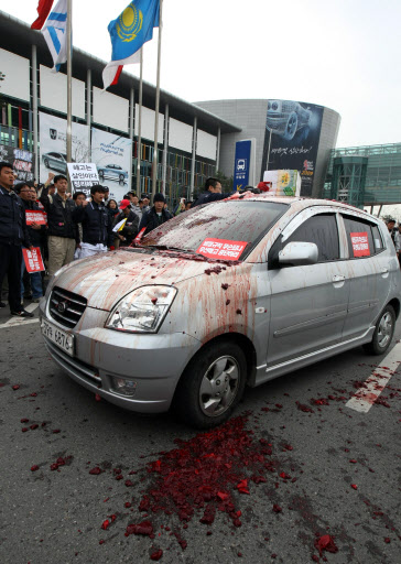  3일 고양시 일산 킨텍스에서 서울모터쇼가 개막된 가운데 전국금속노동조합원들이 행사장 앞에서 기아차 모닝에 소(牛)피를 뿌리는 퍼포먼스를 하고 있다. 조합원들은 현대, 기아, 쌍용, GM대우의 강제휴업 및 대량해고 일자리 빼앗기를 중단하라며 기자회견을 열고 퍼포먼스를 벌이다 전원 출동한 경찰에 연행되었다.   　고양=연합뉴스