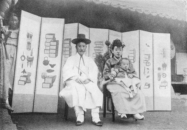 양반집의 잔칫날 풍경을 찍은 사진. 두 내외가 아이를 안고 기념촬영을 하는 장면을 병풍 뒤에서 아낙네가 훔쳐보는 모습이 재미있다.