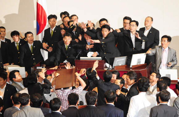 김형오 국회의장으로부터 사회권을 넘겨받은 한나라당 소속 이윤성 국회부의장이 22일 국회 본회의장에서 신문법과 방송법 등 미디어관련법을 표결에 부치자 민주당과 민주노동당 의원들이 거세게 항의하고 있다. 민주당 강기정 의원이 나무판을 이 부의장에게 던지려 하자 국회 경위 등이 이 부의장을 보호하고 있다.  이호정기자 hojeong@seoul.co.kr