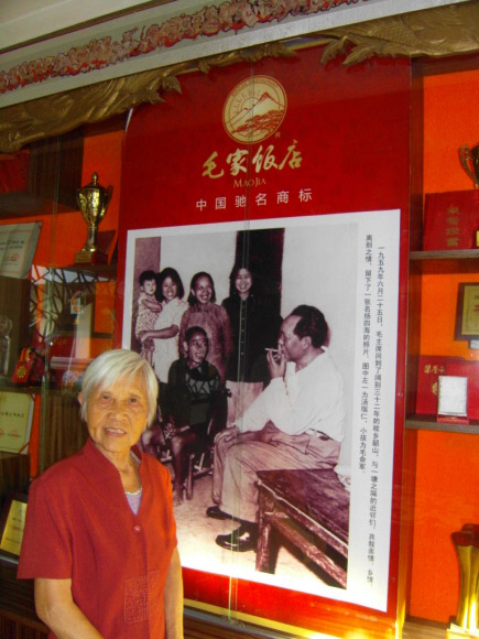 마오자호텔 탕뤼런 회장. 뒤편 사진은 1959년 고향을 방문한 마오쩌둥이 고향사람들과 대화하는 모습을 담은 ‘마오 주석과 고향사람들’로 사진 속 아이를 안고 있는 여성이 탕 회장이다.