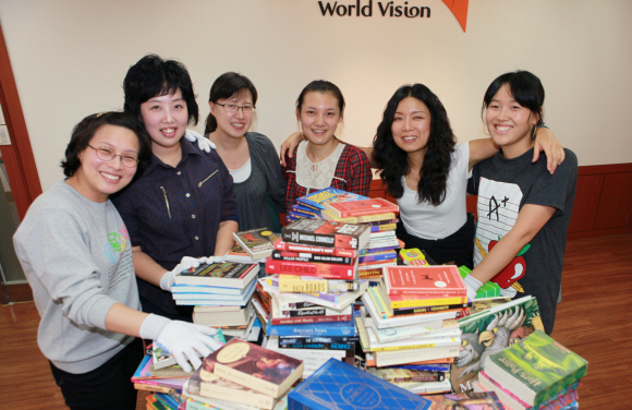 여행작가 오소희(오른쪽 두번째)씨가 30일 서울 여의도 월드비전 건물에서 아프리카 우간다 카삼브야 지역의 도서관에 보낼 책 700여권을 독자들과 함께 포장하며 활짝 웃고 있다. 월드비전 제공