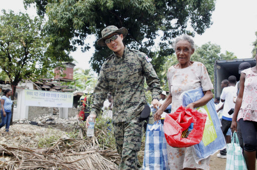 아이티의 재건 및 복구를 위해 파병된 한 단비부대원이 주민과 함께 무거운 짐을 들고 가고 있다. 연합뉴스