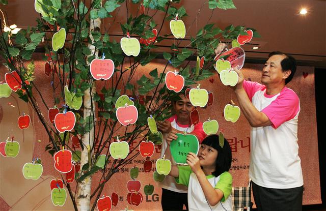 이상철(오른쪽) LG유플러스 부회장 등 임직원과 장애가정 청소년이 17일 열린 ‘두드림 U+’ 프로젝트 출범식에서 미래의 희망을 적은 종이 사과를 나무에 달고 있다. LG유플러스 제공
