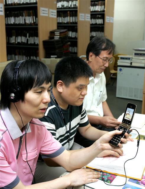 6일 서울 개포동 하상장애인복지관에서 시각장애인들이 자원봉사자(오른쪽)의 도움을 받아 LG유플러스의 시각장애인용 휴대전화로 통화 내용을 확인하고 있다. LG유플러스 제공