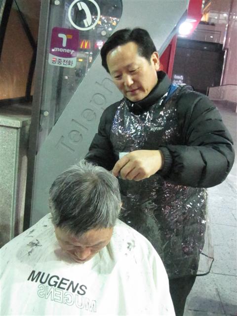 서울 월드컵지구대 소속 천팔용 경위가 지난 27일 오후 서울 영등포역 앞 광장에서 가위로 한 노숙인의 머리를 깎아주고 있다.