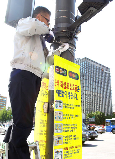 16일 오후 서울 세종로 사거리에서 한 경찰관이 도입이 전면 재검토된 3색 신호등의 홍보 현수막을 떼어 내고 있다. 연합뉴스