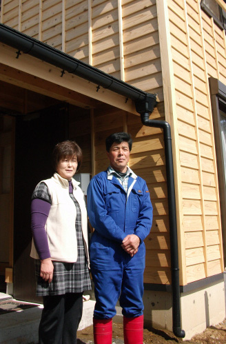 이시노마키시 시라하마에 지은 부흥 주택에서 살고 있는 가쓰야 부부가 집 앞에서 포즈를 취하고 있다.