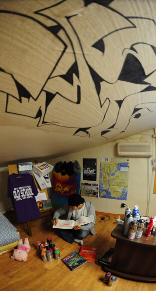 에라원이 자신의 집 다락방에 있는 작업실에서 다음에 그릴 그라피티의 밑그림을 스케치북에 그리고 있다.  