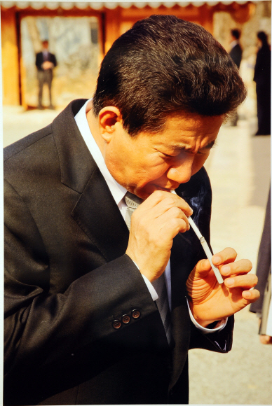 노 전 대통령이 수행원에게 빌린 담배로 담뱃불을 붙이고 있다.