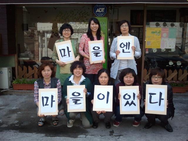 1일 서울 은평구 갈현동 마을n도서관을 운영하는 이미경 대표(아래 줄 왼쪽 두 번째)와 지역 주민들이 ‘마을엔 마을이 있다’라는 글자 카드를 들고 환하게 웃고 있다.