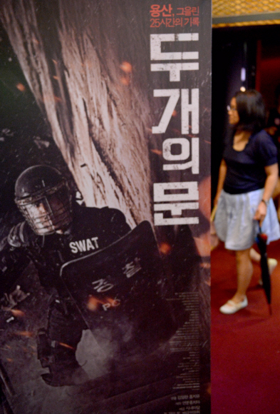 19일 오후 서울 종로구 가든플레이스 상영관 앞에서 한 여성이 용산참사를 다룬 다큐멘터리 영화 ‘두개의 문’ 포스터 옆을 지나가고 있다.  박지환기자 popocar@seoul.co.kr