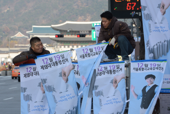 “선거에 꼭 참여하세요”  서울시 선거관리위원회 직원들이 25일 오전 서울 세종로 광화문 일대에서 18대 대통령 선거와 시교육감 재선거 투표 참여를 호소하는 가로등 현수막을 설치하고 있다. 도준석기자 pado@seoul.co.kr