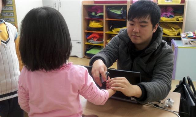 27일 오후 서울 마포구의 한 어린이집에서 현장 등록원이 노트북에 연결된 장치를 이용해 여자 어린이의 지문을 채취하고 있다. 