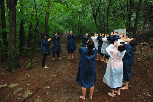 맨발에 비옷을 입은 숲 치유 프로그램 참가자들이 산림치유 운영요원의 설명에 맞춰 산림욕 기체조를 따라하고 있다.