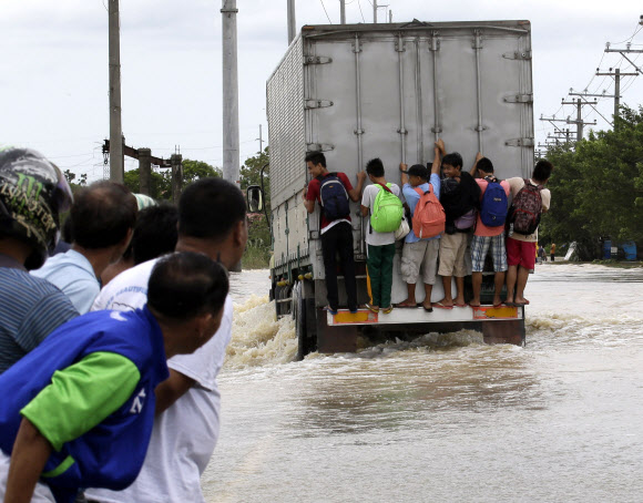 지난 12일 제25호 태풍 ‘나리’가 강타한 필리핀 북부 불라칸주 산일데폰소의 도로가 홍수로 인해 강으로 변한 가운데 학생들이 가방을 멘 채 대형 트럭 뒤에 매달려 집으로 돌아가는 모습을 시민들이 바라보고 있다.  산일데폰소 AP 연합뉴스