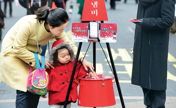 구세군 자선냄비가 지난 2일부터 시종식과 함께 본격적인 모금을 시작한 가운데 서울 중구 명동에서 한 시민이 아이의 손을 잡고 냄비에 성금을 넣고 있다. 