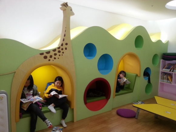 세종도서관 지하 1층 어린이 도서관에서 아이들이 나무 모양 의자에 앉아 책을 읽고 있다.
