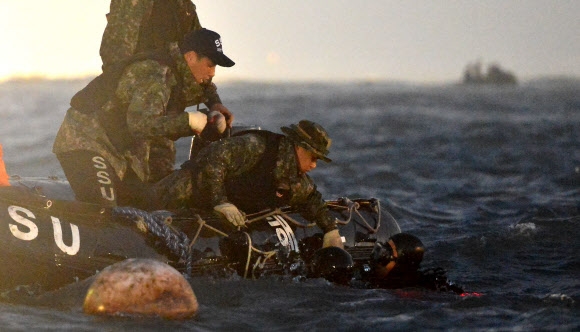 합동구조팀 잠수사들이 세월호 침몰 1주일째인 지난 22일 저녁 동료의 도움을 받아 현장 수색작업을 벌이고 있다. 연합뉴스
