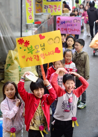 어버이날인 8일 경기 광명시 광명전통시장에서 광명초등학교 학생들이 부모님에 대한 감사함을 적은 손팻말을 들고 웃으며 행진하고 있다. 이날 열린 ‘870! 광명 반짝이 사랑의 카네이션 행사’는 어린이에게 효의 의미를 전달하고, 전통시장에 대한 친밀도를 높여 지역 공동체와 하나가 되는 기회를 제공하기 위해 마련됐다. 정연호 기자 tpgod@seoul.co.kr