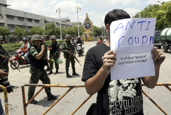 군부 쿠데타가 일어난 태국 방콕의 민주기념탑 근처에서 23일 한 시민이 계엄군이 지켜보는 가운데 ‘쿠데타 반대’라고 적힌 종이를 들고 시위를 하고 있다. 방콕 AP 연합뉴스 