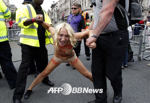 7일(현지시간) 영국 런던 중심부 국회의사당 앞 광장에서 우크라이나 여성 인권단체 피멘(femen) 회원들이 상의를 탈의한 채 여성할례(FGM)를 반대하는 반누드시위를 벌이던 중 마주한 카메라 앞에서 시니컬한 웃음을 짓고 있다.  ⓒ AFPBBNews=News1