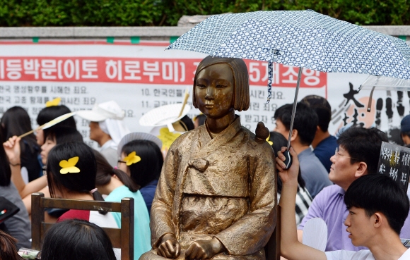 6일 서울 종로구 주한 일본대사관 앞에서 열린 일본군 위안부 문제 해결을 위한 정 기 수요집회에서 한 참석자가 소녀상에게 우산을 씌워주고 있다.  박윤슬 기자 seul@seoul.co.kr