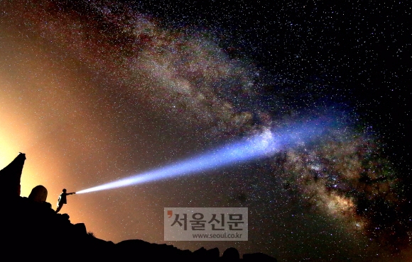 15일 강원도 정선의 밤하늘에 가득한 은하수 사이로 한 청년이 손전등으로 하늘을 비추고 있다.(캐논 1DX, 8-15mm어안렌즈, 조리개4, 25초, ISO 5000으로 촬영) 박지환 기자 popocar@seoul.co.kr
