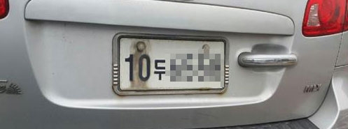 납품 단가가 낮아 녹 방지를 하지 않은 볼트와 너트를 사용한 정부 봉인 때문에 녹물이 흐른 한 자동차 뒤 번호판.