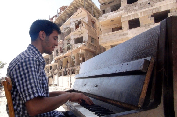 지난해 6월 시리아 수도 다마스쿠스 외곽 야르무크에 있는 팔레스타인 난민 캠프에서 연주하던 ‘시리아 피아노맨’ 아이함 아흐마드의 모습. 그는 자신이 치고 있던 피아노가 이슬람 무장세력에 의해 불타 없어지자 고국을 떠나기로 결심했다. 다마스쿠스 AFP 연합뉴스