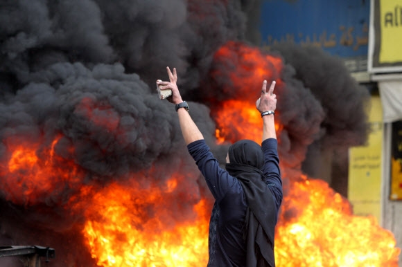 10일(현지시간) 팔레스타인 서안 헤브론에서 팔레스타인 시위대와 이스라엘 경찰의 충돌로 검은 연기와 화염이 난무하는 가운데 한 팔레스타인인이 돌을 들고 승리의 V 포즈를 취하고 있다. 헤브론 AFP 연합뉴스 