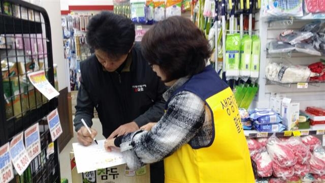 강동구 생명지킴이 자원봉사자가 번개탄 판매업소에 희망 판매소 동참 서명을 받는 모습.  강동구 제공 