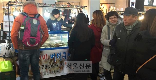 지난 16일 오후 6시 30분 서울 중구 명동 노점상 앞에서 관광객들이 음식이 완성되기를 기다리고 있다.