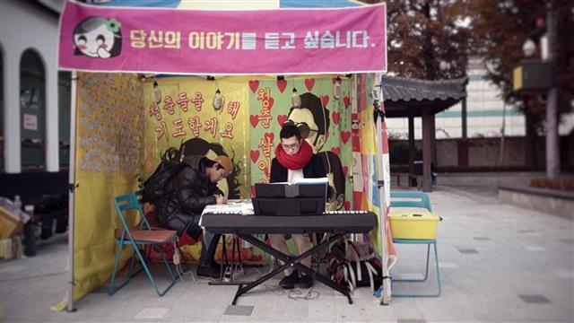 2013년 11월 서울 동작구 대방동 지하철 1호선 대방역 인근 쌈드림 부스에서 최현우(오른쪽)씨가 피아노 연주를 하는 사이 한 남성이 위로 엽서를 쓰고 있다. 쌈드림 제공
