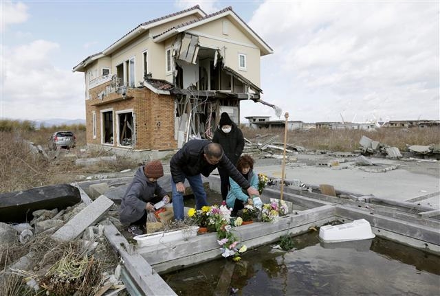 지난해 3월 11일 동일본 대지진 4주년을 맞아 일본 후쿠시마현 나미에시에서 한 가족이 숨진 부모님을 추모하는 꽃다발을 놓고 있다.  EPA 연합뉴스