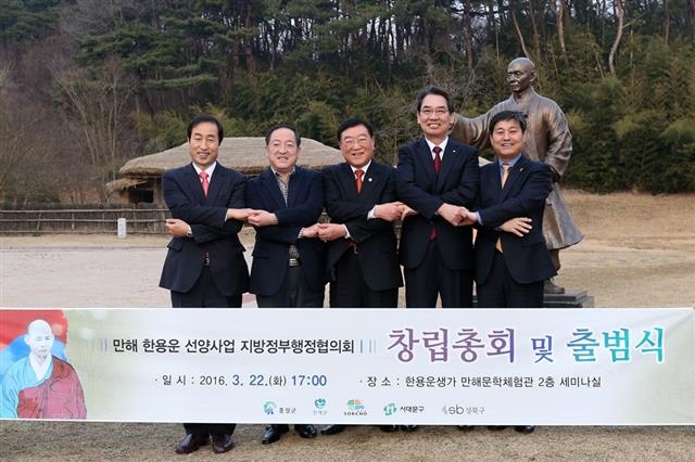 문석진(왼쪽부터) 서대문구청장, 이병선 속초시장, 김석환 홍성군수, 이순선 인제군수, 김영배 성북구청장이 만해 한용운의 생가와 동상 앞에서 손을 맞잡고 있다. 성북구 제공
